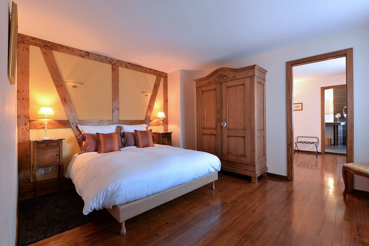 A bedroom with a large bed, wooden wardrobe, and a mirror above the bed.