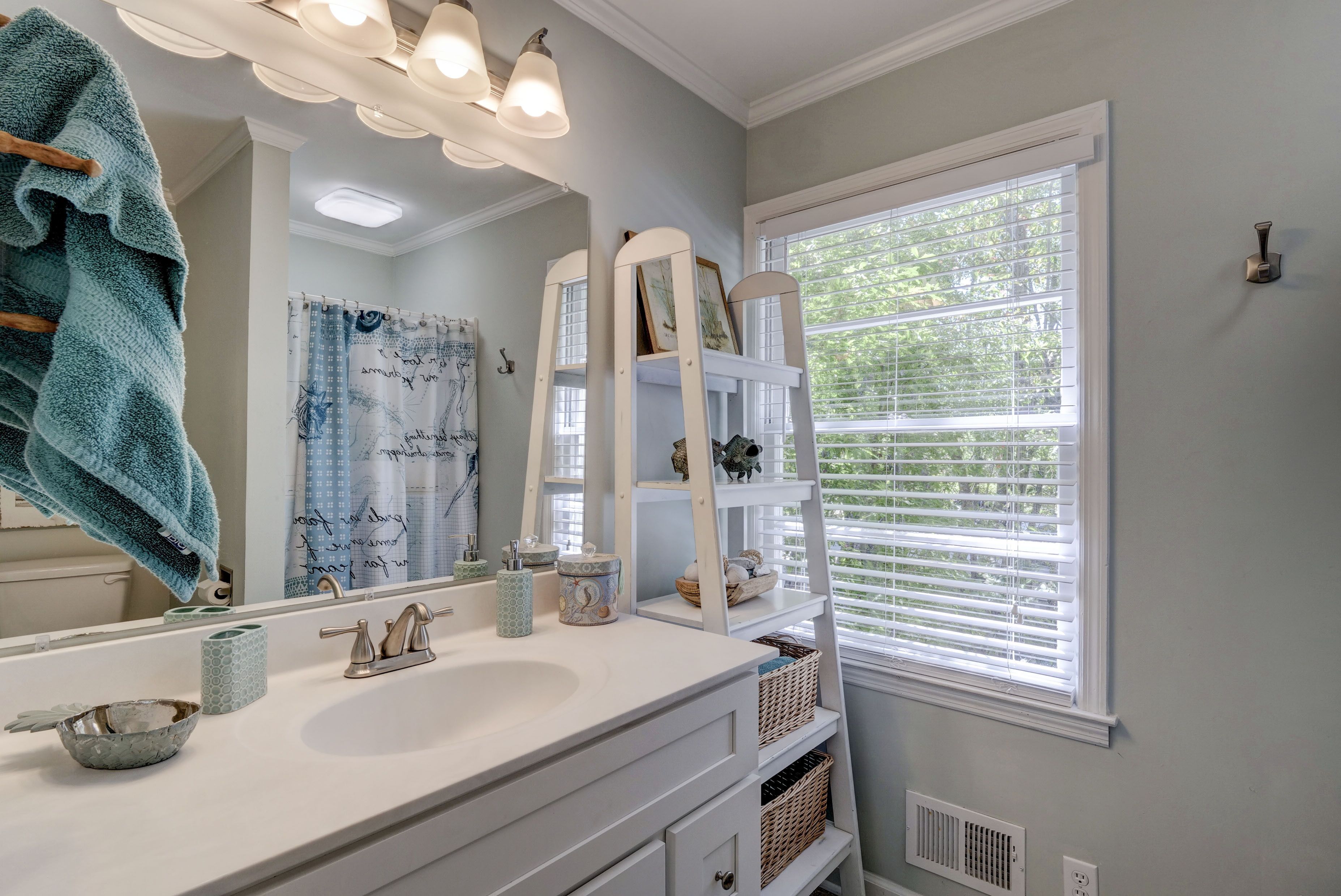 A bathroom with a white vanity, a large mirror, and a window with blinds.