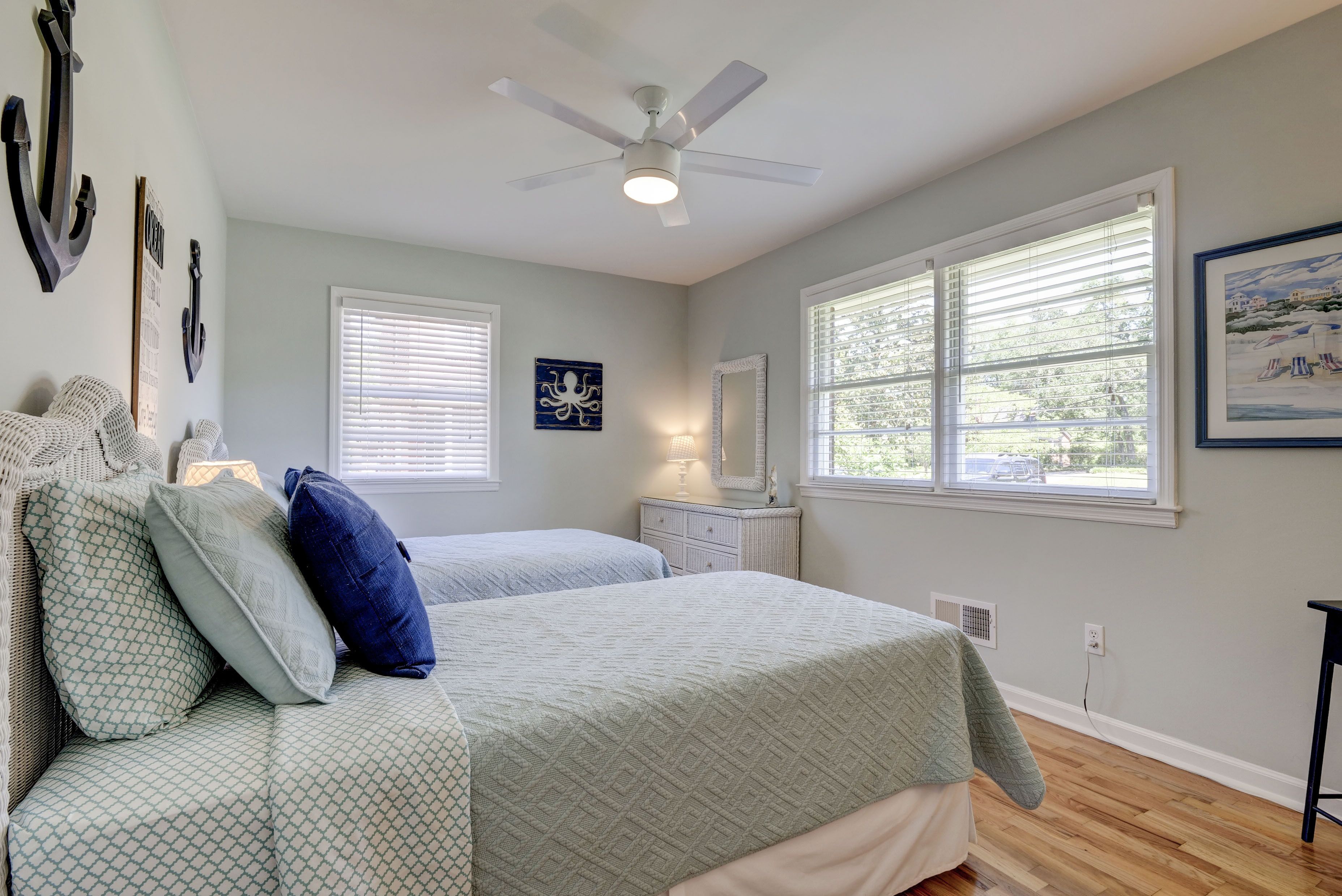 Une chambre avec deux lits, un ventilateur de plafond, une fenêtre avec des stores et des éléments de décoration fixés au mur.