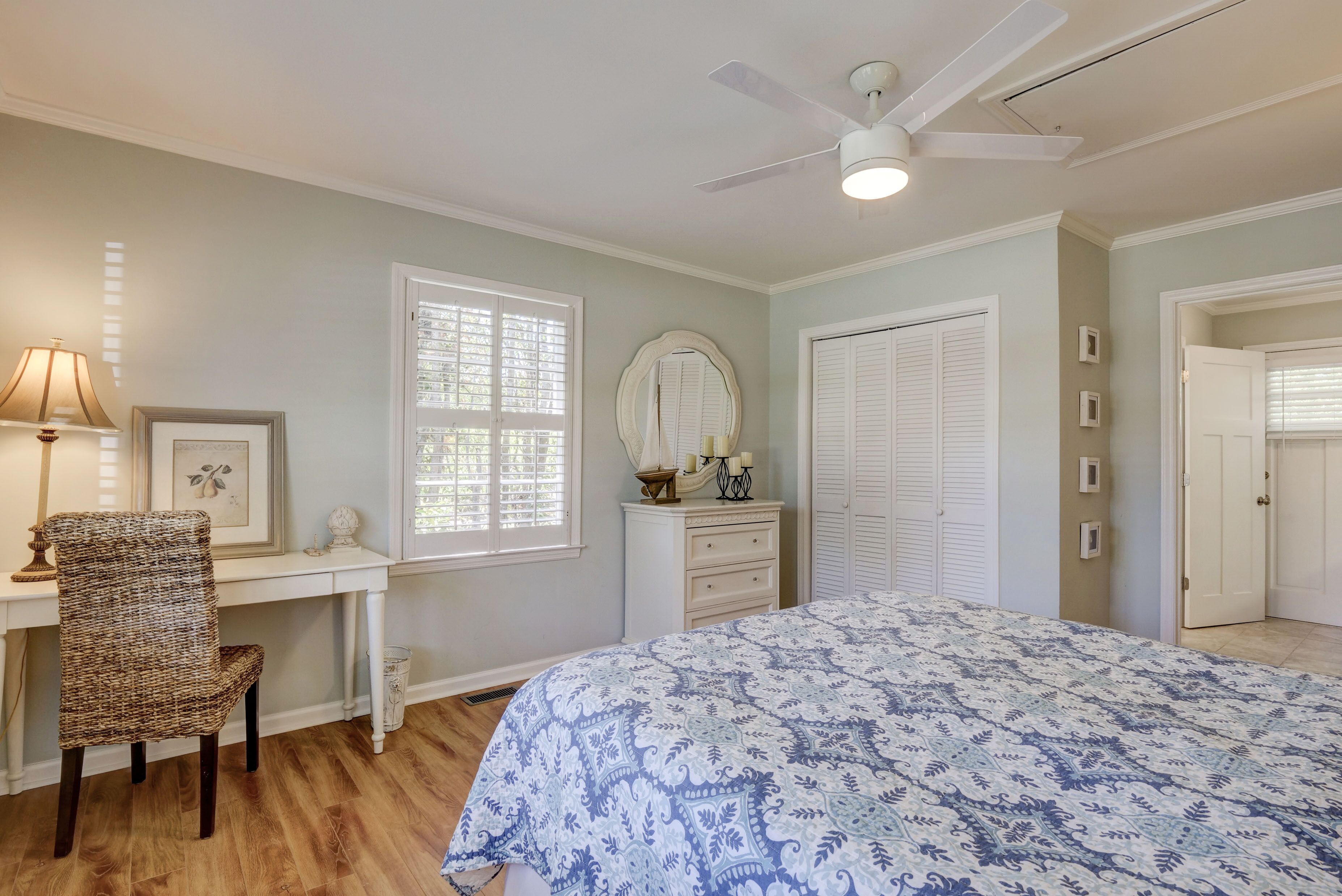 Une chambre à coucher comprenant un lit, un bureau, une chaise, un ventilateur de plafond et une fenêtre avec des stores.