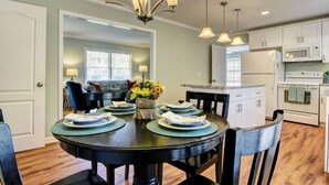 A dining area with a round table set for four, surrounded by chairs. A chandelier hangs above, and the room has wooden flooring. - Beautiful, Charming, Historic Riverfront and Wrightsville Beach! (Wilmington)