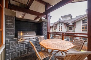 Een terras buiten met een stenen openhaard, een roestvrijstalen barbecue en houten meubels.