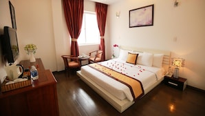 Une chambre d’hôtel avec un grand lit, un bureau avec un téléphone, une chaise, une petite table ornée d’un vase de fleurs et un tableau au mur.