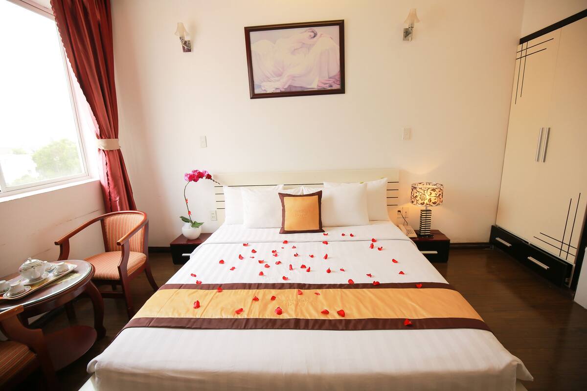 Habitació d'hotel amb un llit ben fet, una cadira, una taula petita amb una safata i una finestra amb cortines.