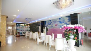 Un hall d’hôtel avec des chaises blanches, un grand arrangement floral et une fresque représentant des nuages.