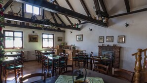 Un comedor con mesas y sillas de madera, una chimenea de ladrillo y un techo alto con vigas a la vista.