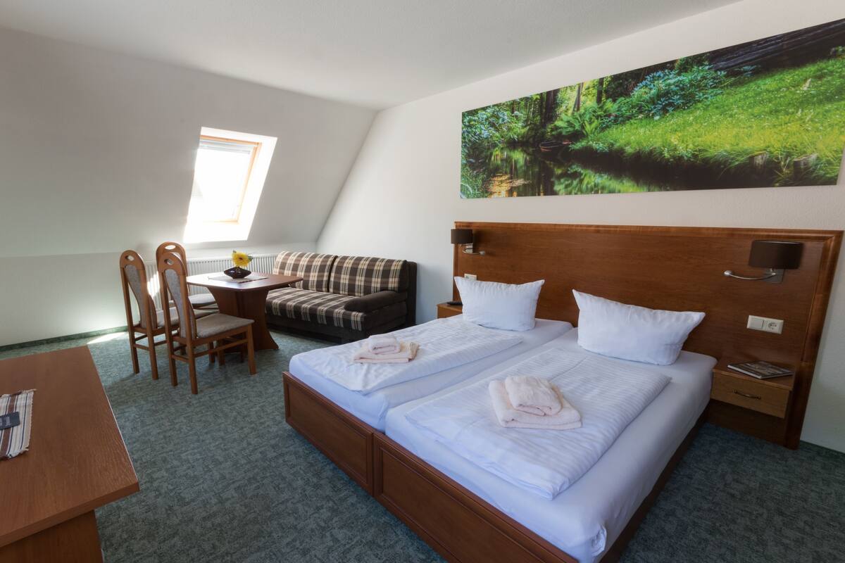 A hotel room with a large bed, a sofa, a desk, and a painting of a forest.