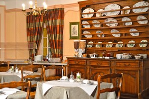 A dining area with wooden tables, chairs, and a china cabinet with plates. - Hôtel de l'Ange (Niedermorschwihr)