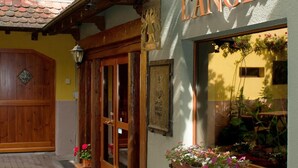 L’entrée d’un hôtel, avec une porte en bois, une enseigne indiquant « HÔTEL de L’ANGE » et des jardinières sur les rebords des fenêtres.