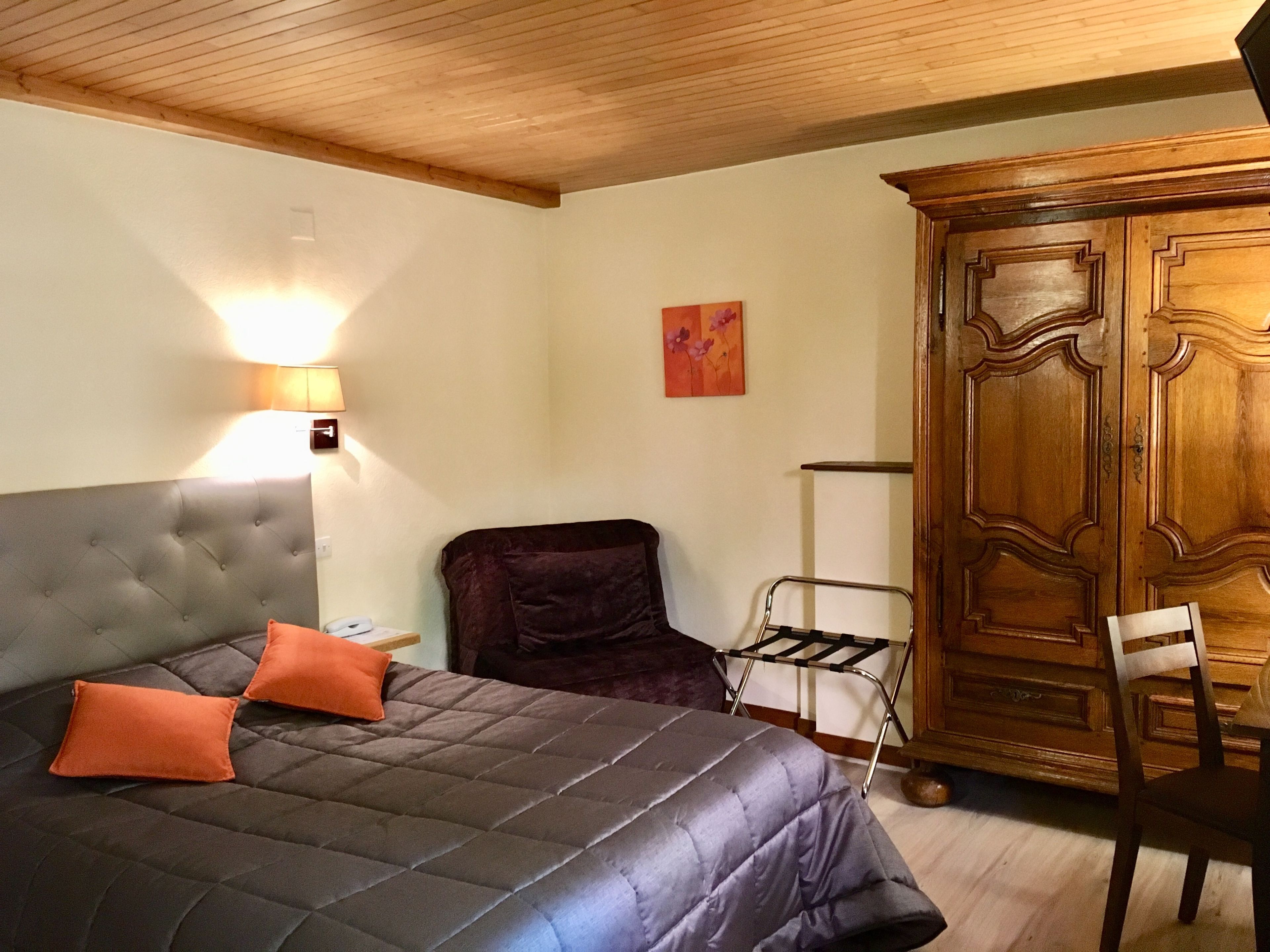 Un dormitorio con una cama, un armario, una silla y una lámpara fijada a la pared.