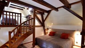 Une chambre avec un escalier en bois, un lit avec des oreillers rouges et un plafond en pente.