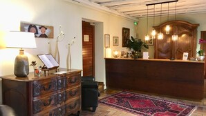 Un espace d’accueil avec un bureau en bois, un fauteuil en cuir noir, un tapis rouge à motifs et un plafond avec des poutres apparentes.