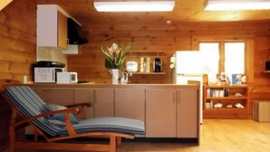 A cozy cabin interior with a wooden floor, a kitchenette with a microwave, a sink, and a shelf with books and decorative items. - YOISAMA Sunrise Beach House (Ishigaki)