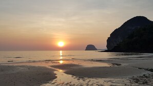 A beach with a sunset, calm sea, and a prominent rock formation. - Mook Ing Lay (Ko Mook)
