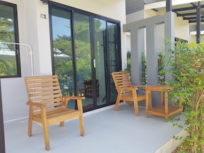A balcony with two wooden chairs and a small table, a sliding glass door, and a potted plant. - Mook Ing Lay (Ko Mook)