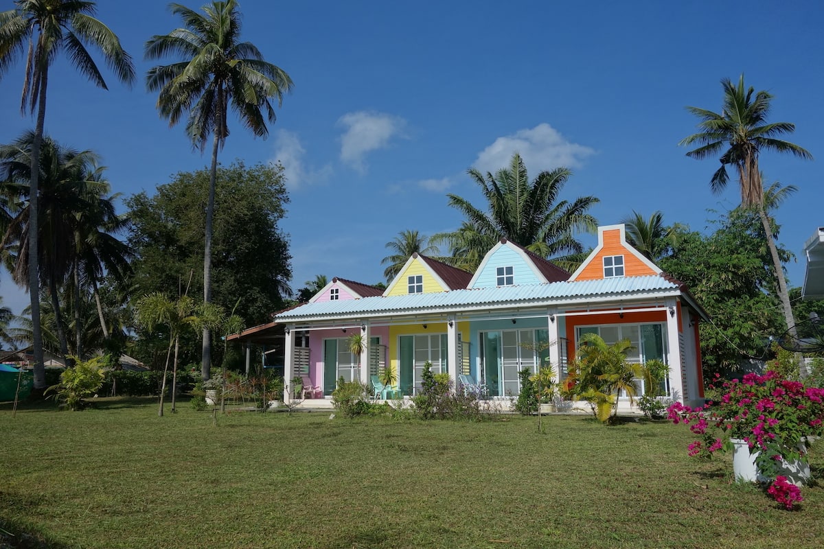 A colorful house with a well-maintained lawn and palm trees in the background.