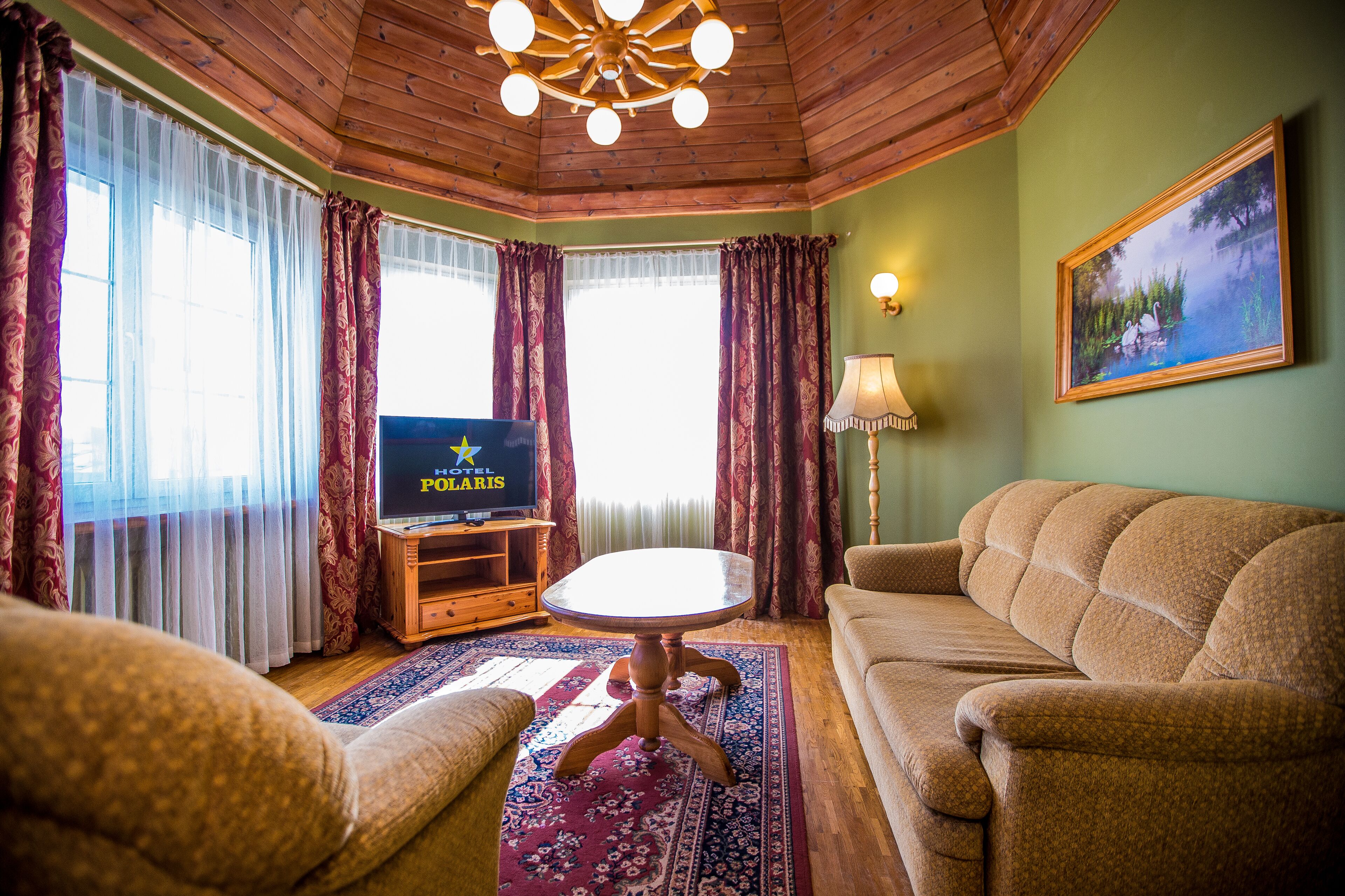 Un salon chaleureux avec un plafond en bois, un téléviseur à écran plat posé sur un meuble en bois, une table basse ronde et un canapé beige.