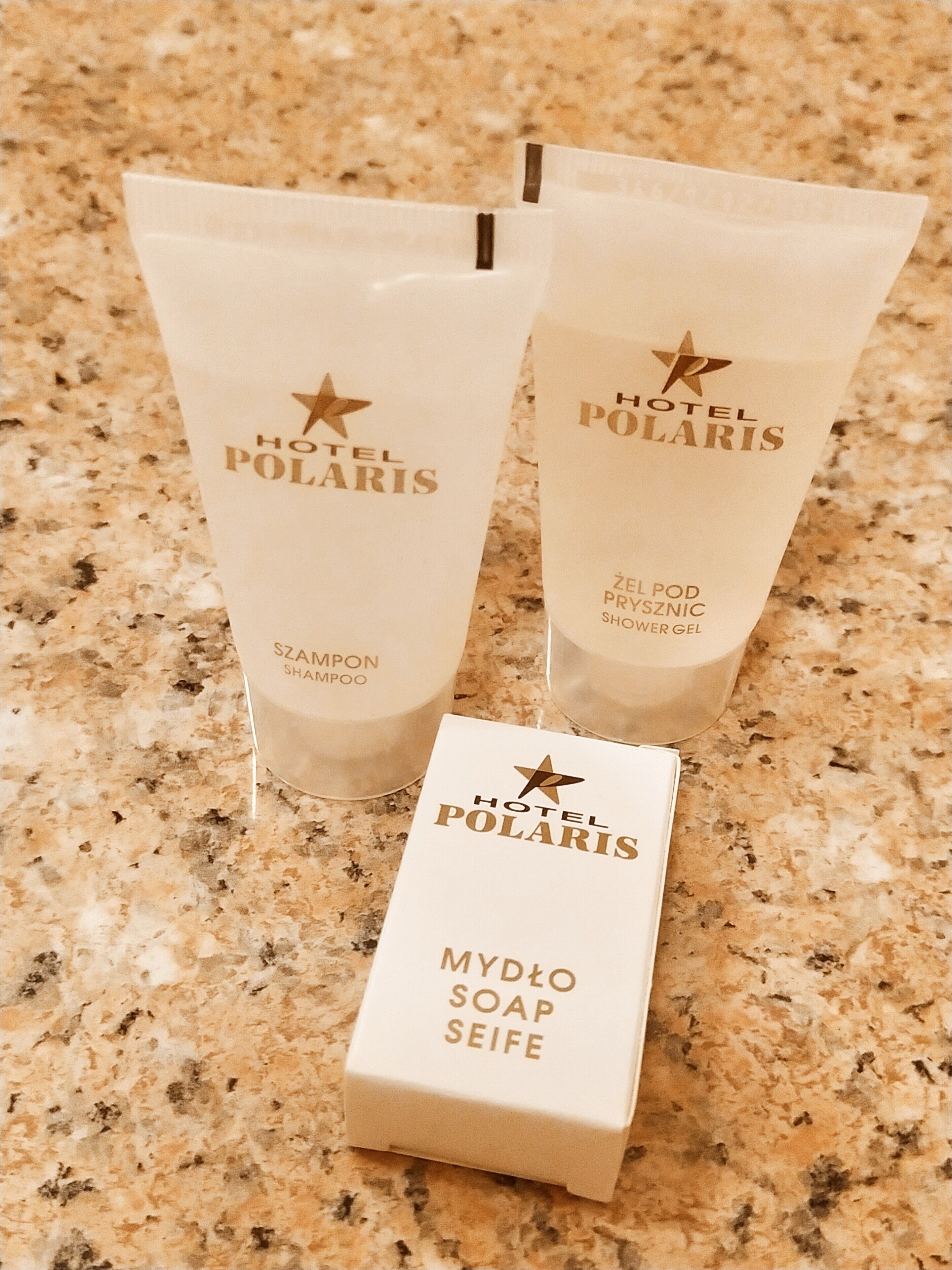 Three Hotel Polaris branded shampoo and conditioner tubes and a soap box on a granite countertop.