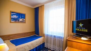 A hotel room with a bed, a television displaying the hotel name, a painting on the wall, and a window with curtains.