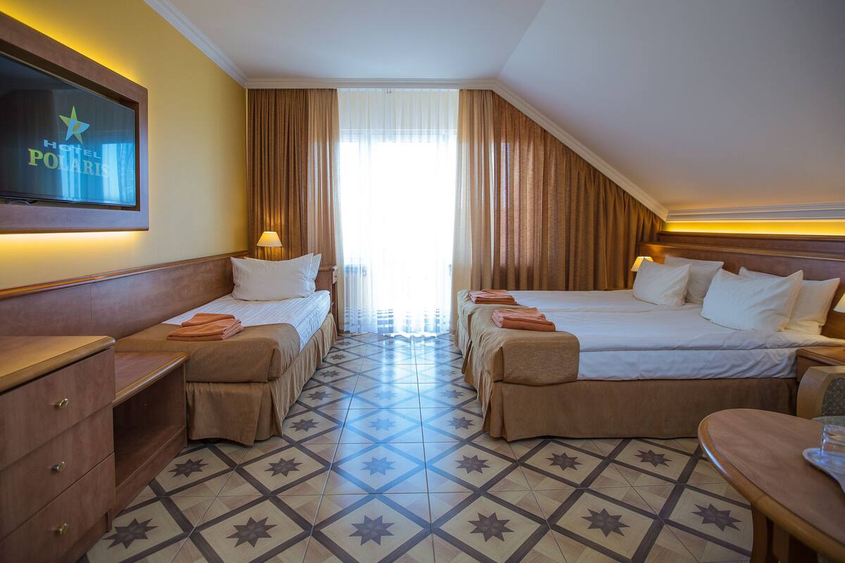 Habitación de hotel con dos camas, un televisor en la pared y un ventanal con cortinas.