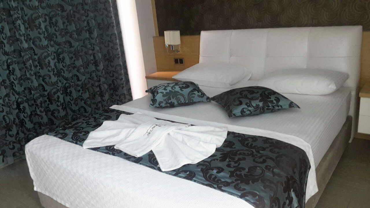 A neatly made bed with patterned bedding, a bedside table with a lamp, and a patterned curtain.