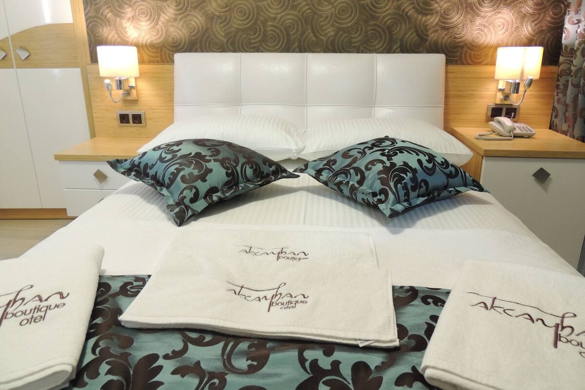 A hotel room with a white bed, two patterned pillows, a bedside table with a lamp, and a nightstand with a phone.