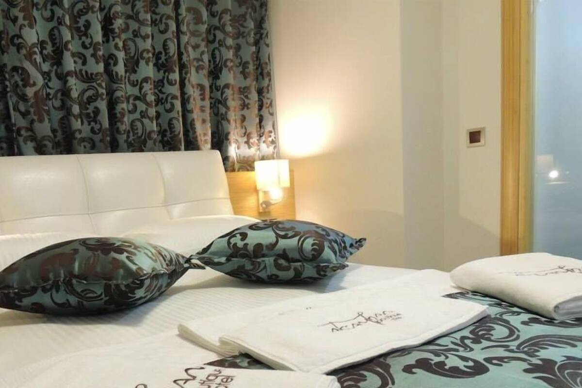 A hotel room with a bed, patterned curtains, a headboard, and a bedside lamp.