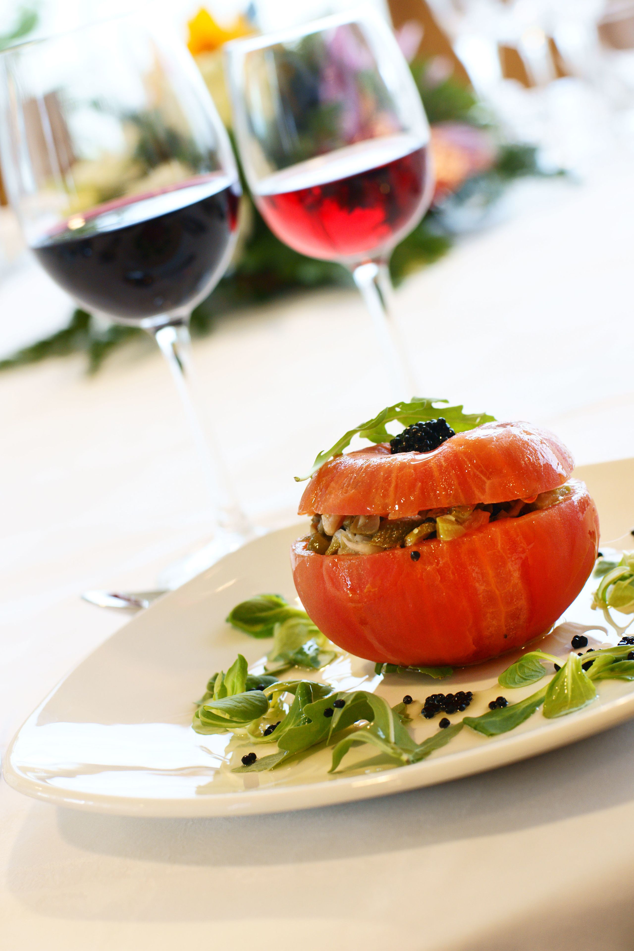 Un plato con un tomate relleno y una copa de vino tinto.