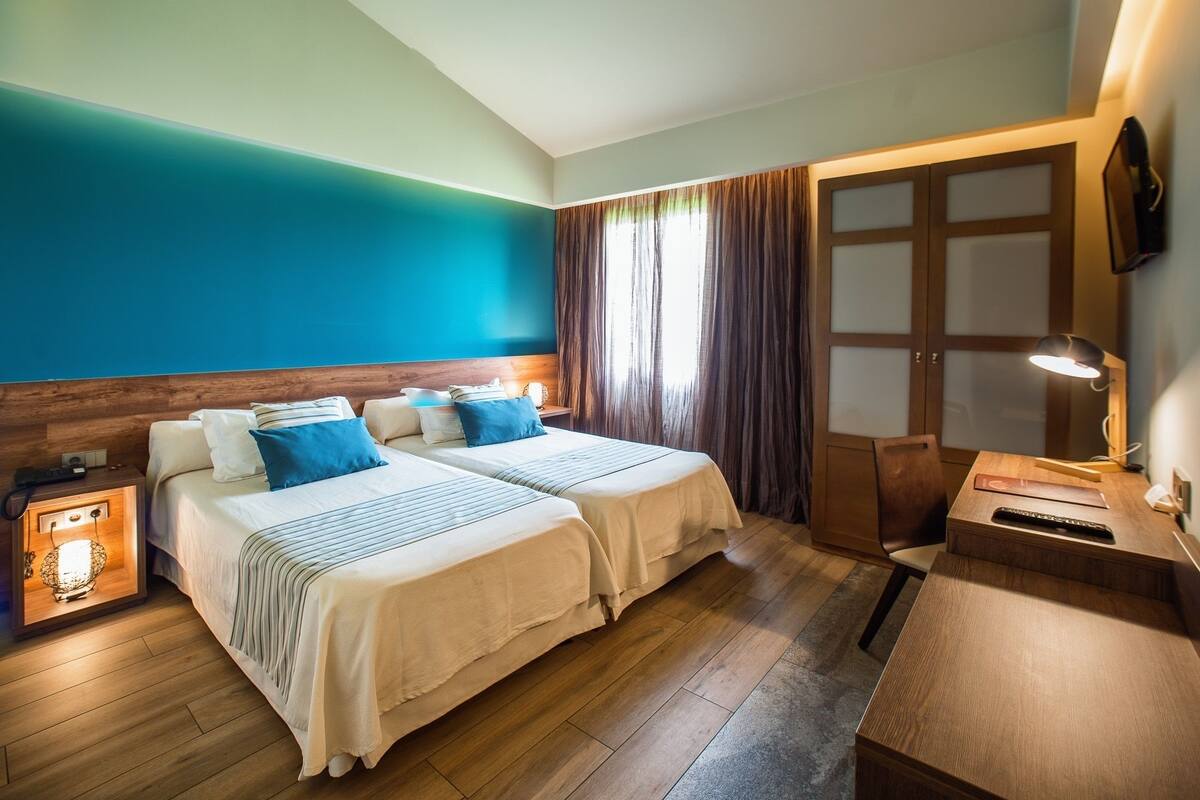 Une chambre d’hôtel avec deux lits, un bureau, une chaise, une table de chevet et une armoire.