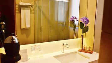 Un baño con un espejo grande, un lavabo, una ducha y un florero con flores.