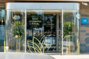 A modern hotel entrance with glass doors, a Wi-Fi sign, and potted plants.