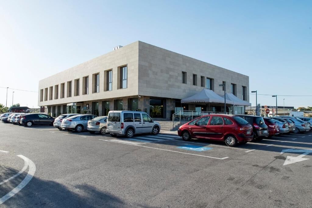 Un parking avec plusieurs voitures, un bâtiment doté d’un toit plat et un ciel dégagé.
