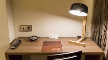 A wooden desk with a remote control, a bowl of snacks, a lamp, a brochure, and a sign indicating no smoking.