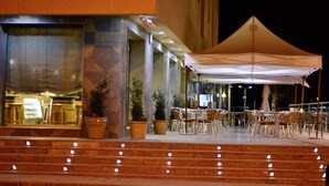 An outdoor seating area with tables and chairs, a covered section with a canopy, and steps leading up to the entrance. - Hotel Venta Baños (Murcia)