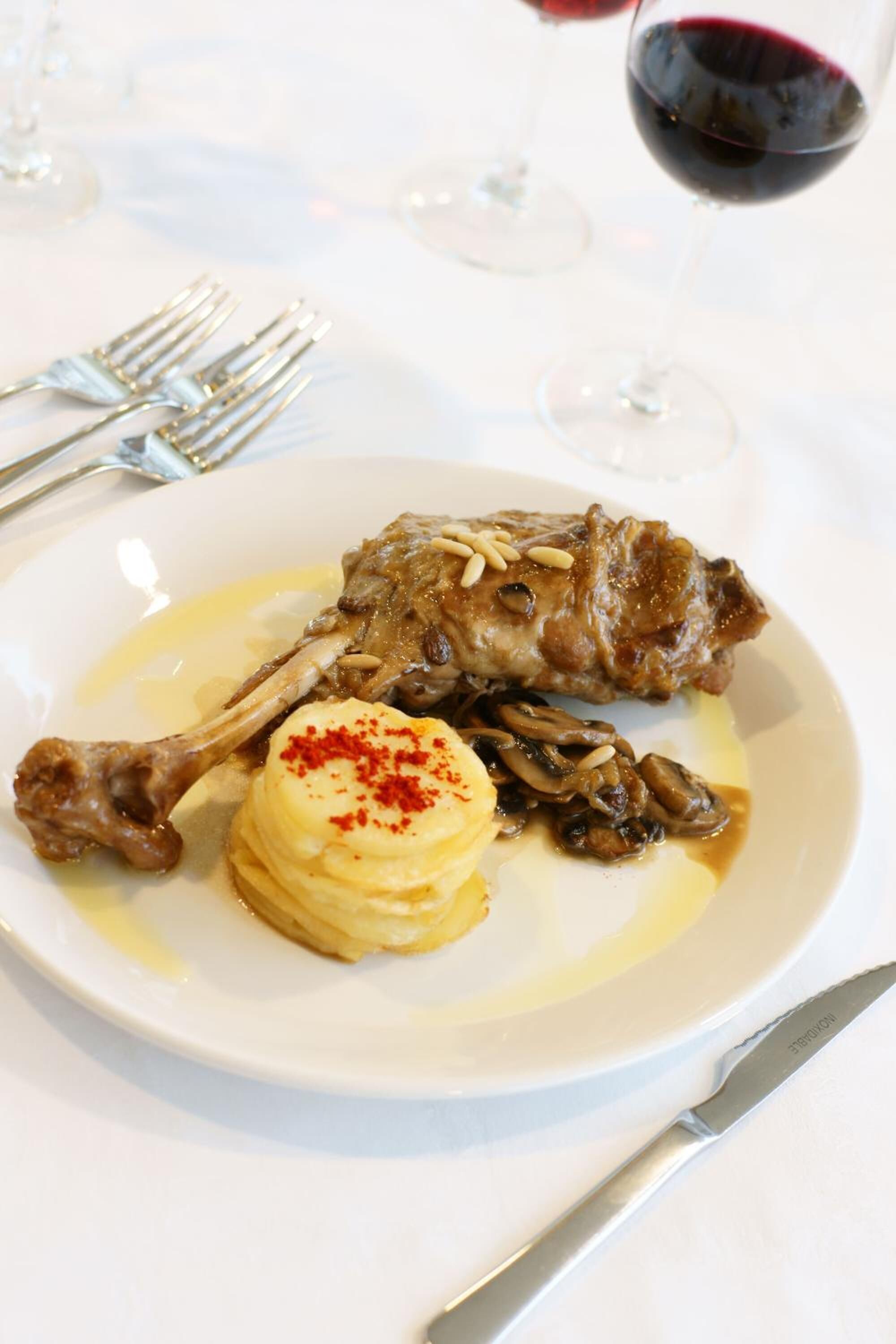 Un plato con un palillo de cordero, puré de papas y champiñones salteados.