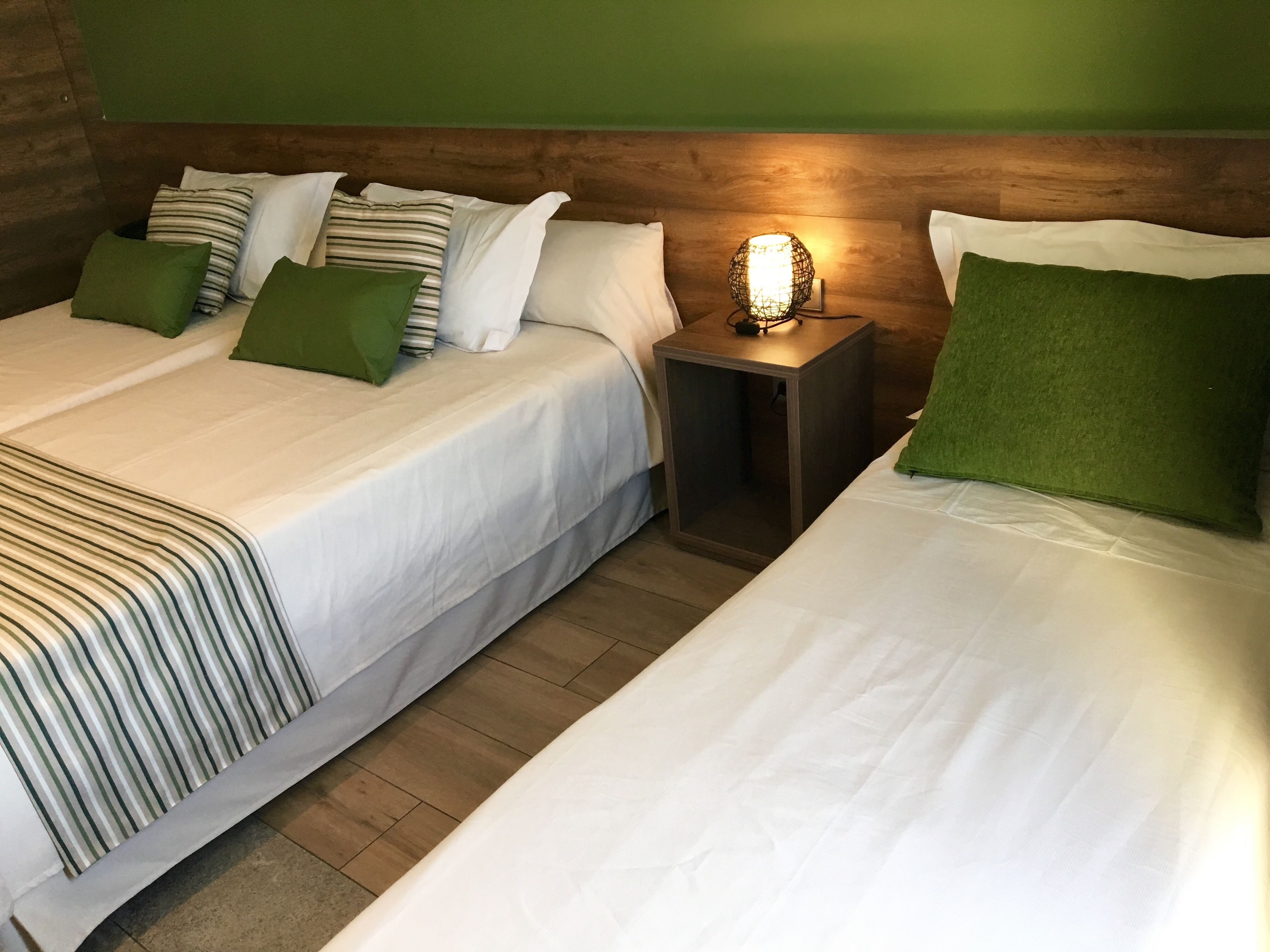 A hotel room with two beds, a nightstand with a lamp, and green pillows.