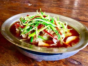 Kulho keittoa, jossa on kasviksia ja lihaa, puupöydällä.