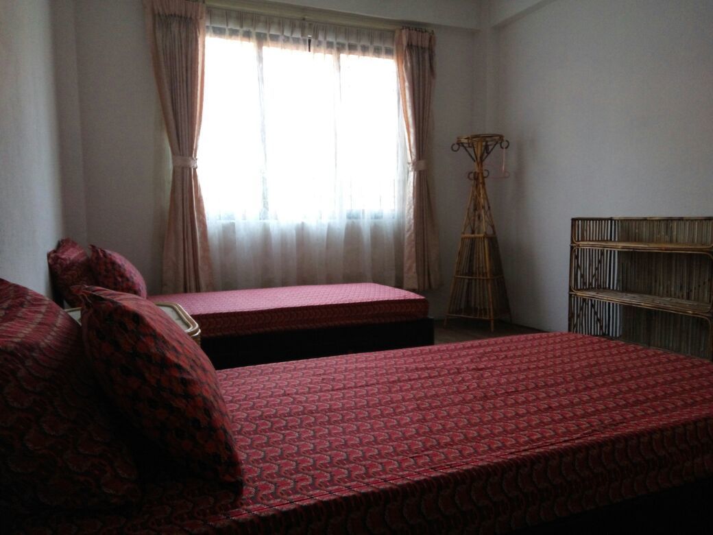 Una habitación con dos camas, una ventana con cortinas, un perchero de madera y un estante en la pared.