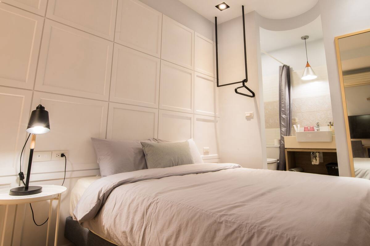 A modern bedroom with a bed, bedside table, lamp, and a large mirror.
