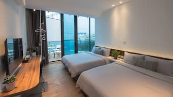 A modern hotel room with two beds, a wooden desk, a TV, and a balcony with a city view.