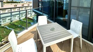 A modern outdoor balcony with a table and chairs, large windows, and a view of the cityscape. - Galilee (Magong)