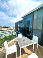 A modern outdoor balcony with a table and chairs, large windows, and a view of the cityscape.