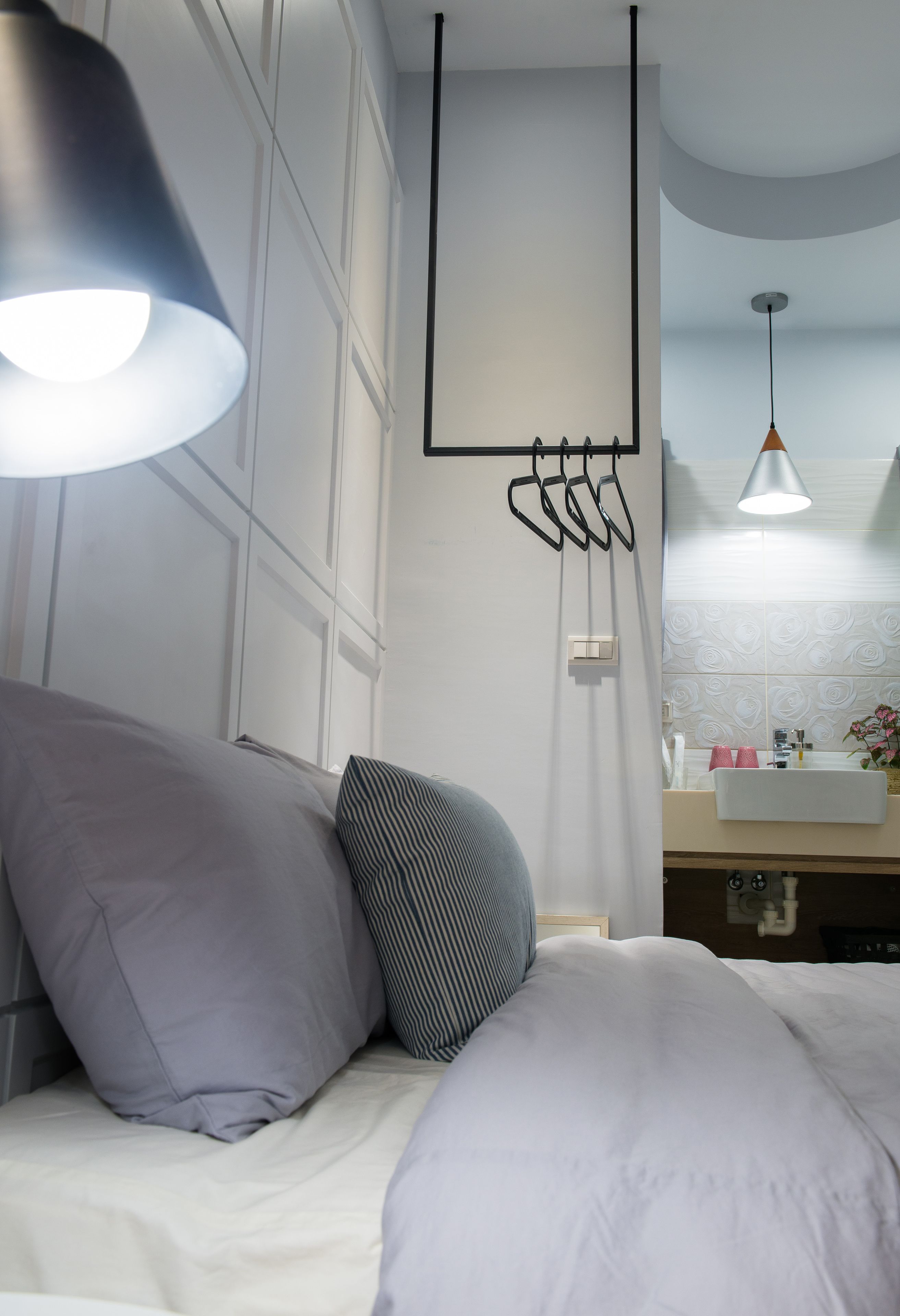 A modern bedroom with a bed, pillows, a hanging light fixture, a mirror, and a sink.