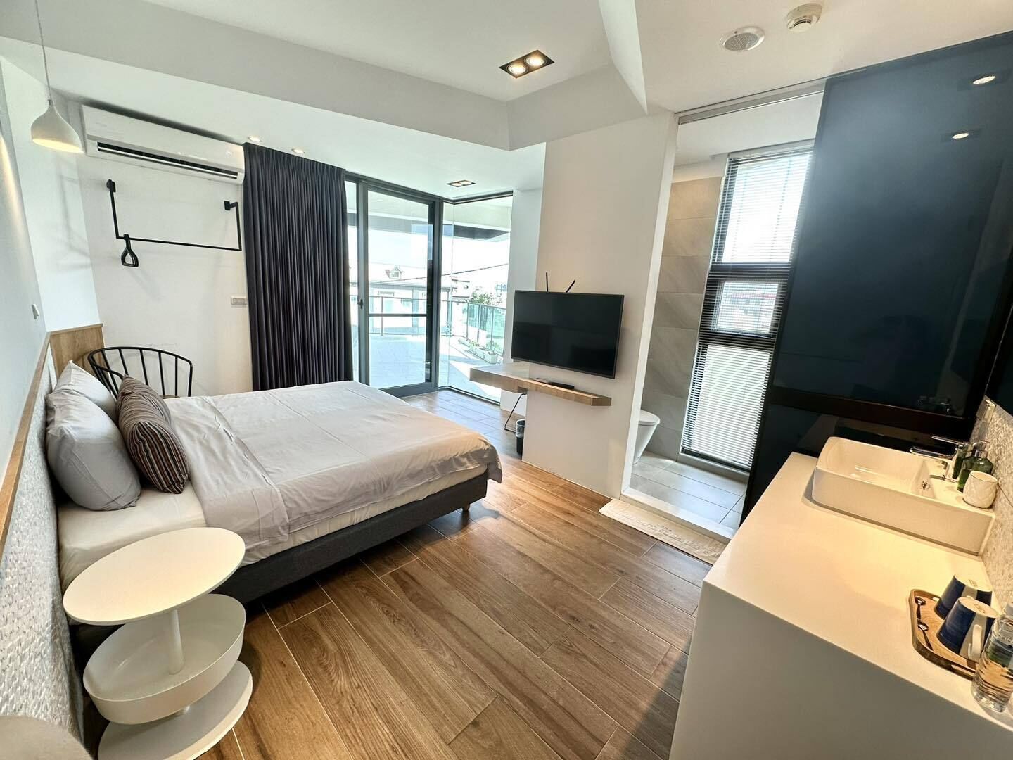 A modern bedroom with a bed, a TV, a bathroom with a sink, and a large window.