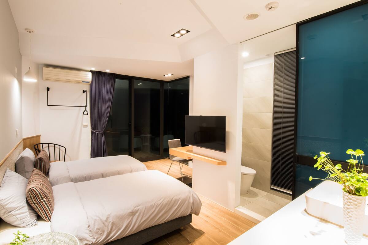 A modern bedroom with two beds, a desk, and a TV.