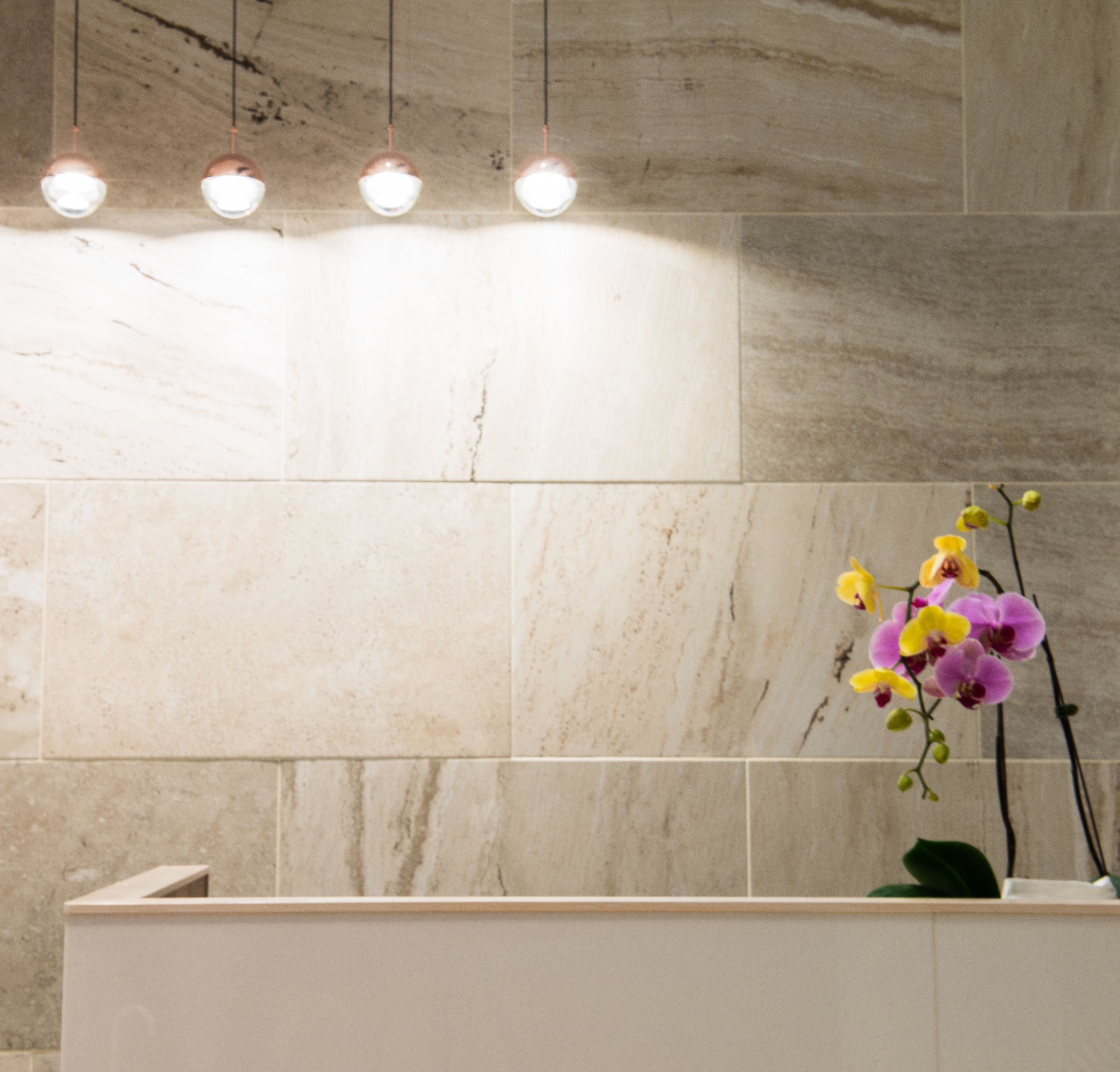 A bathroom with marble tiles, a white sink, and a vase with orchids.