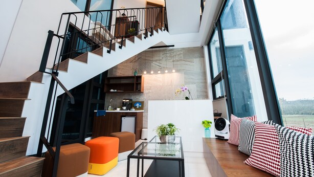 A modern interior with a staircase leading to an upper level, a seating area with a glass coffee table, and a view through large windows. - Galilee (Magong)