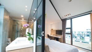 A modern hotel room with a large bed, a bathroom with a glass shower, and a view of the city through large windows. - Galilee (Magong)