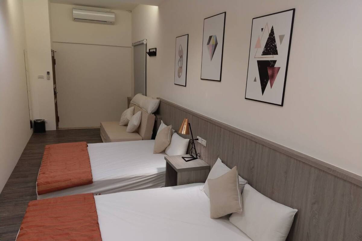Habitación de hotel con dos camas, una mesita de noche, una lámpara y cuadros en la pared.