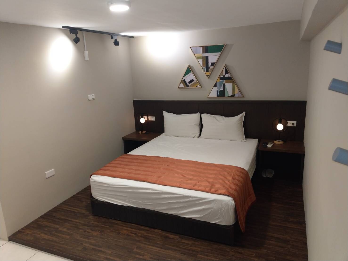 A modern hotel room with a large bed, two bedside tables, a ceiling light, and a wall-mounted artwork.